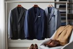 A modern wardrobe scene showing several suit jackets in different colors with leather shoes and a pocket square, suggesting a curated nine-suit men’s collection.